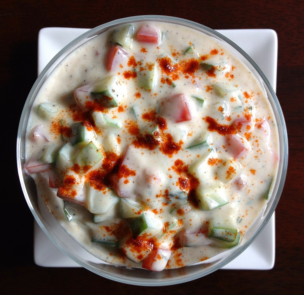 Bowl of Indian raita with yogurt, cucumber, tomatoes, and fresh mint, with a touch of cumin and paprika