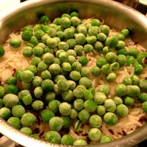 Adding frozen peas to almost-cooked basmati rice in a saucepan on stovetop